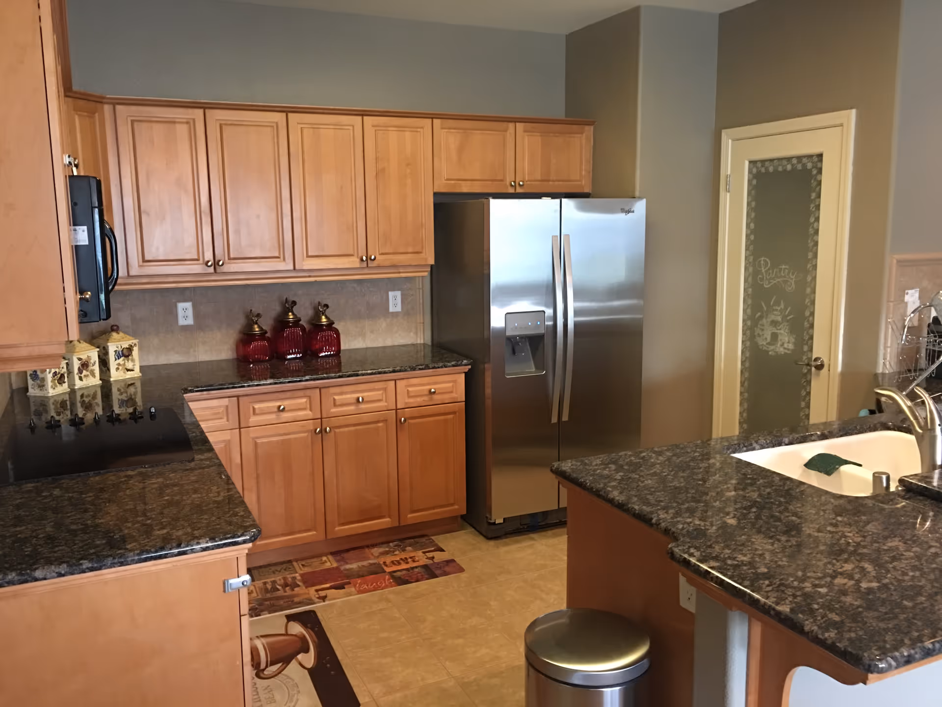 Modern kitchen in a senior living facility with wooden cabinets, granite countertops, stainless fridge, island