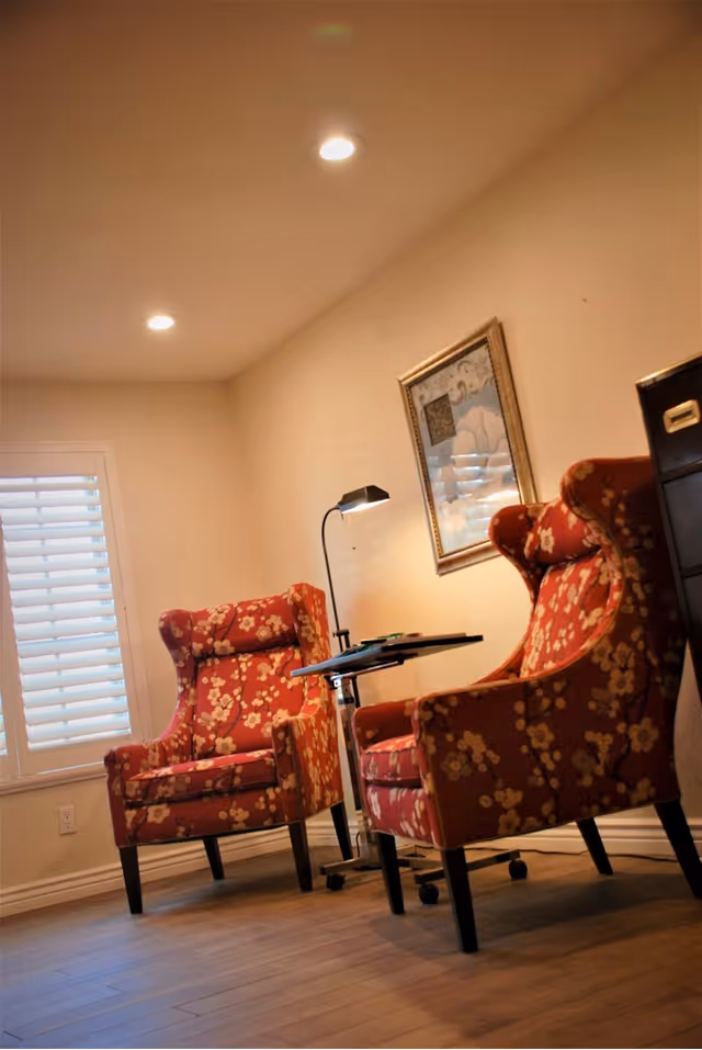 Two floral armchairs flank a small table and lamp in a cozy lounge.