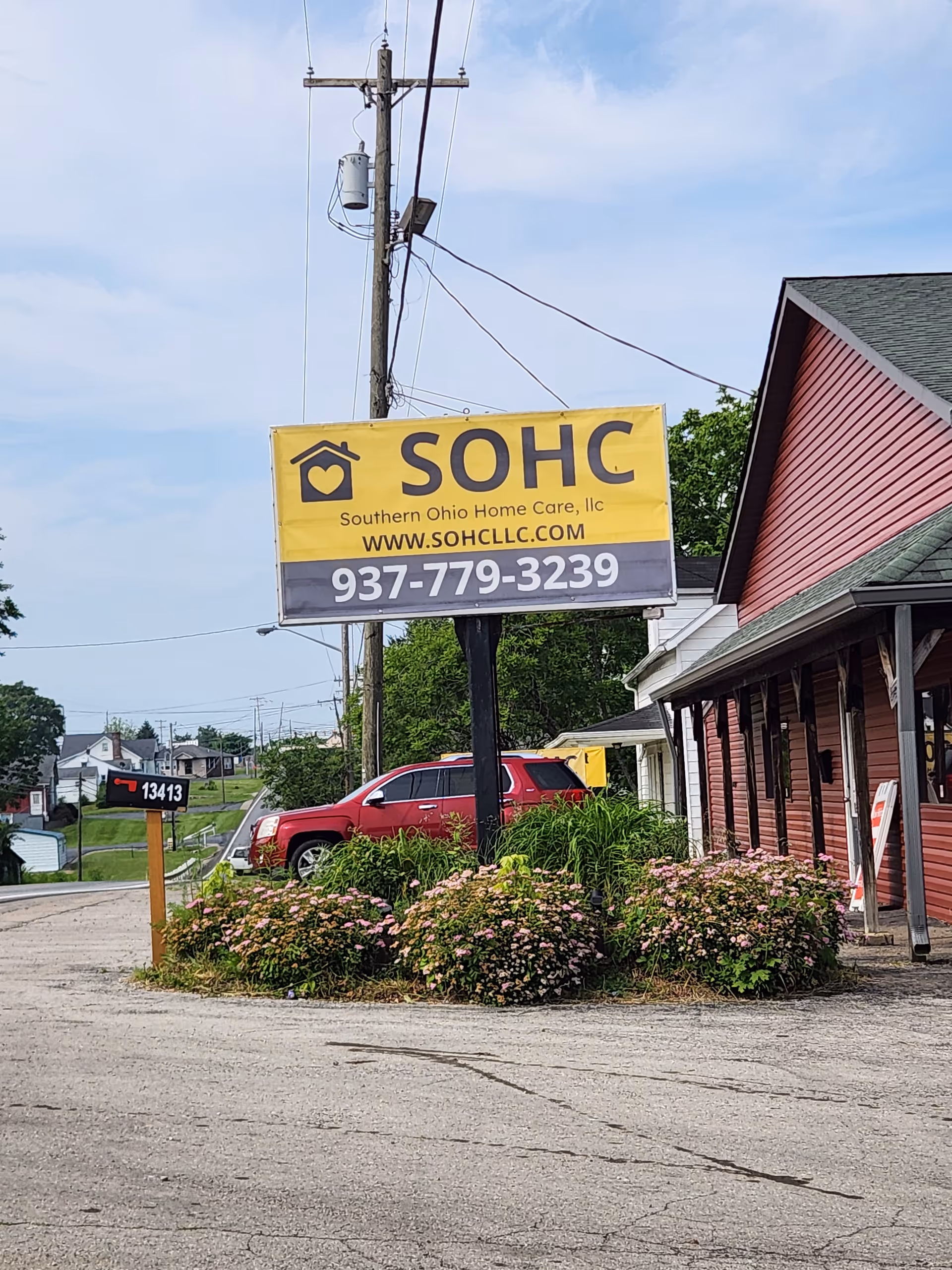 Yellow SOHC sign for Southern Ohio Home Care on a pole beside a pink building.