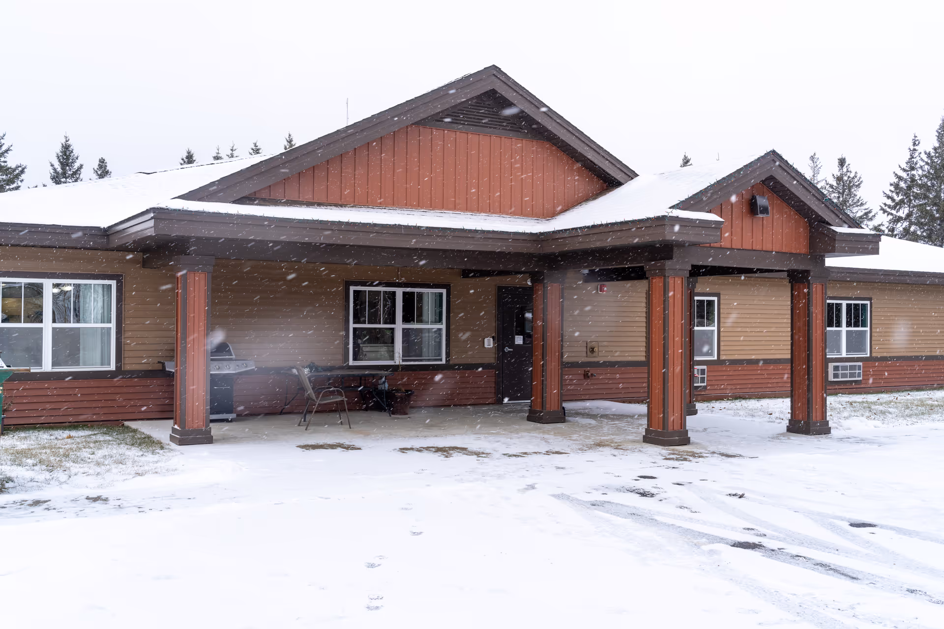 Snow-covered, single-story senior living facility front with a covered porch and seating.