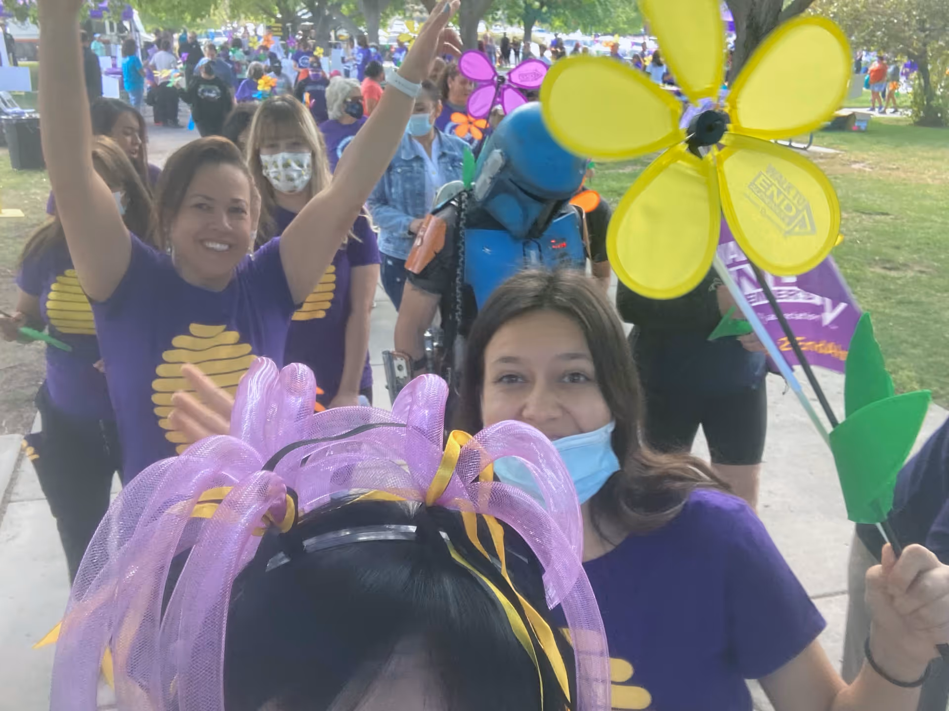 Group of people in purple shirts outdoors, celebrating with colorful pinwheels and balloons.