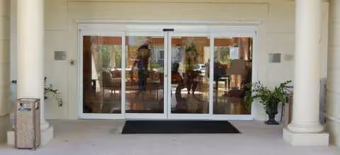 Glass double doors lead to a bright lobby with seating; silhouettes of people inside.