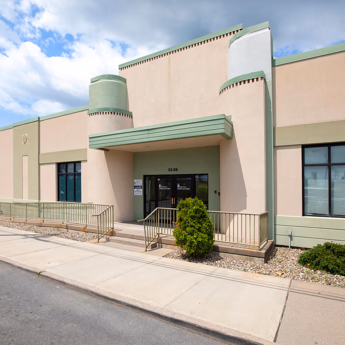 Exterior view of a beige medical building entrance with green accents and ramps