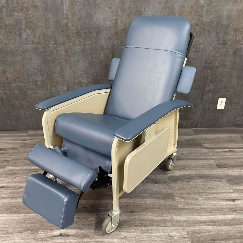 Blue padded reclining chair with leg support on wheels in a clinical room.