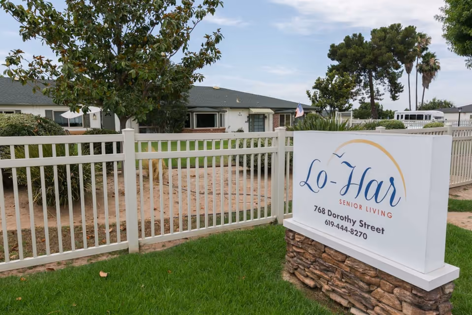 White sign reading 'Lo-Har Senior Living' in front of a fenced single-story building with lawn and trees.