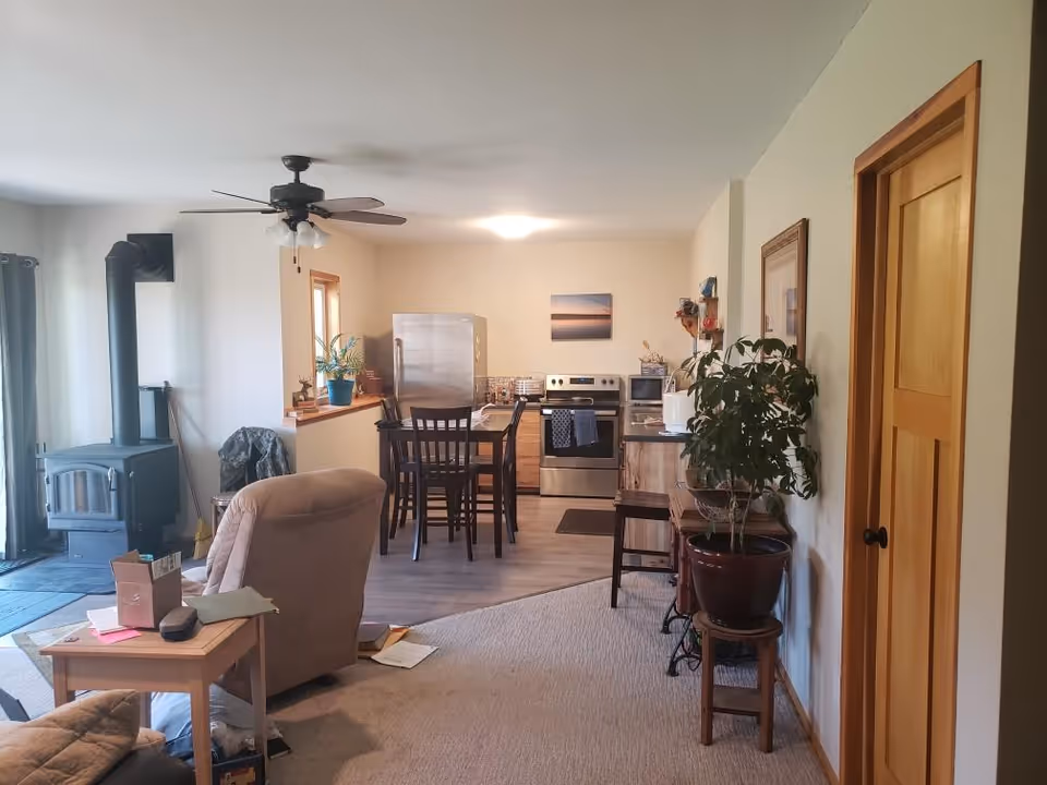 Open-concept living area with sofa, dining table, kitchen appliances, and a wood stove.
