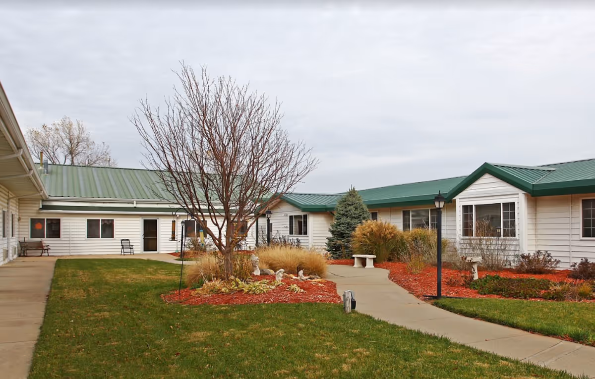Exterior view of Franklin Meadows senior living facility with white siding, green roof, and landscaped courtyard.