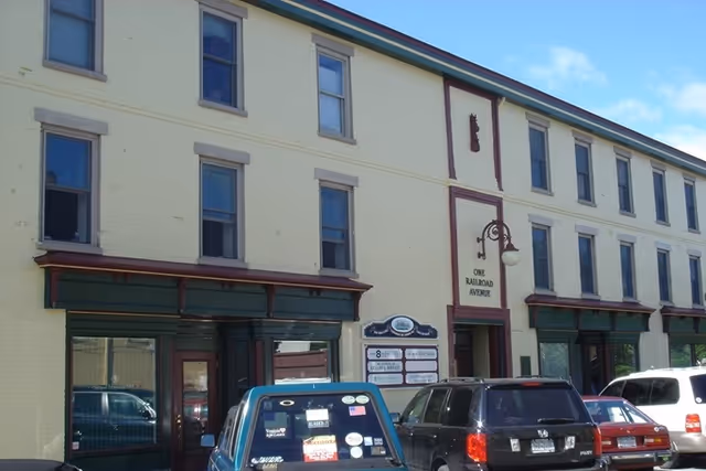 Yellow brick building front with windows, storefronts, and parked cars along the street.