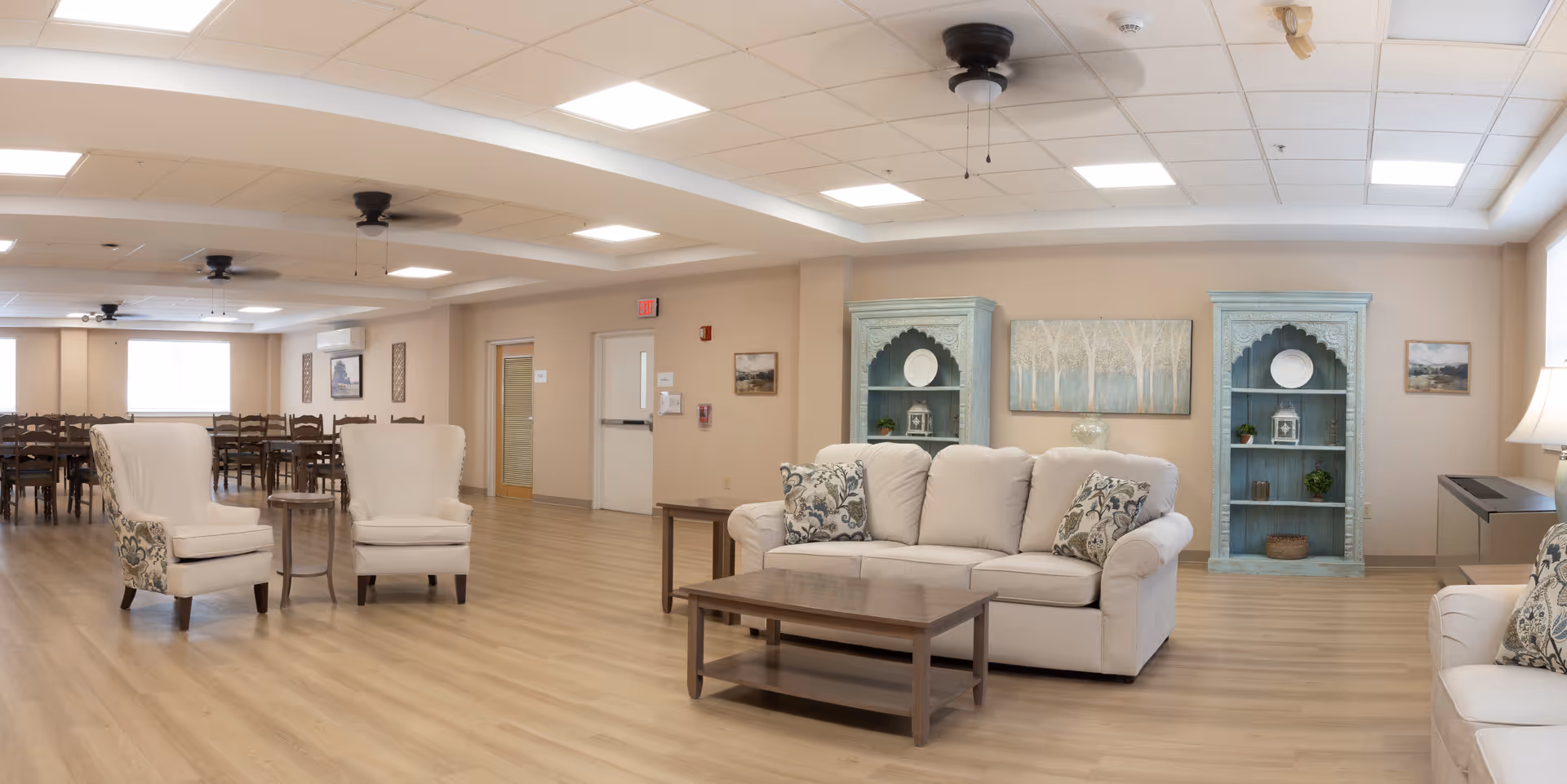 Spacious assisted living common area with sofas, chairs, and a dining area in background