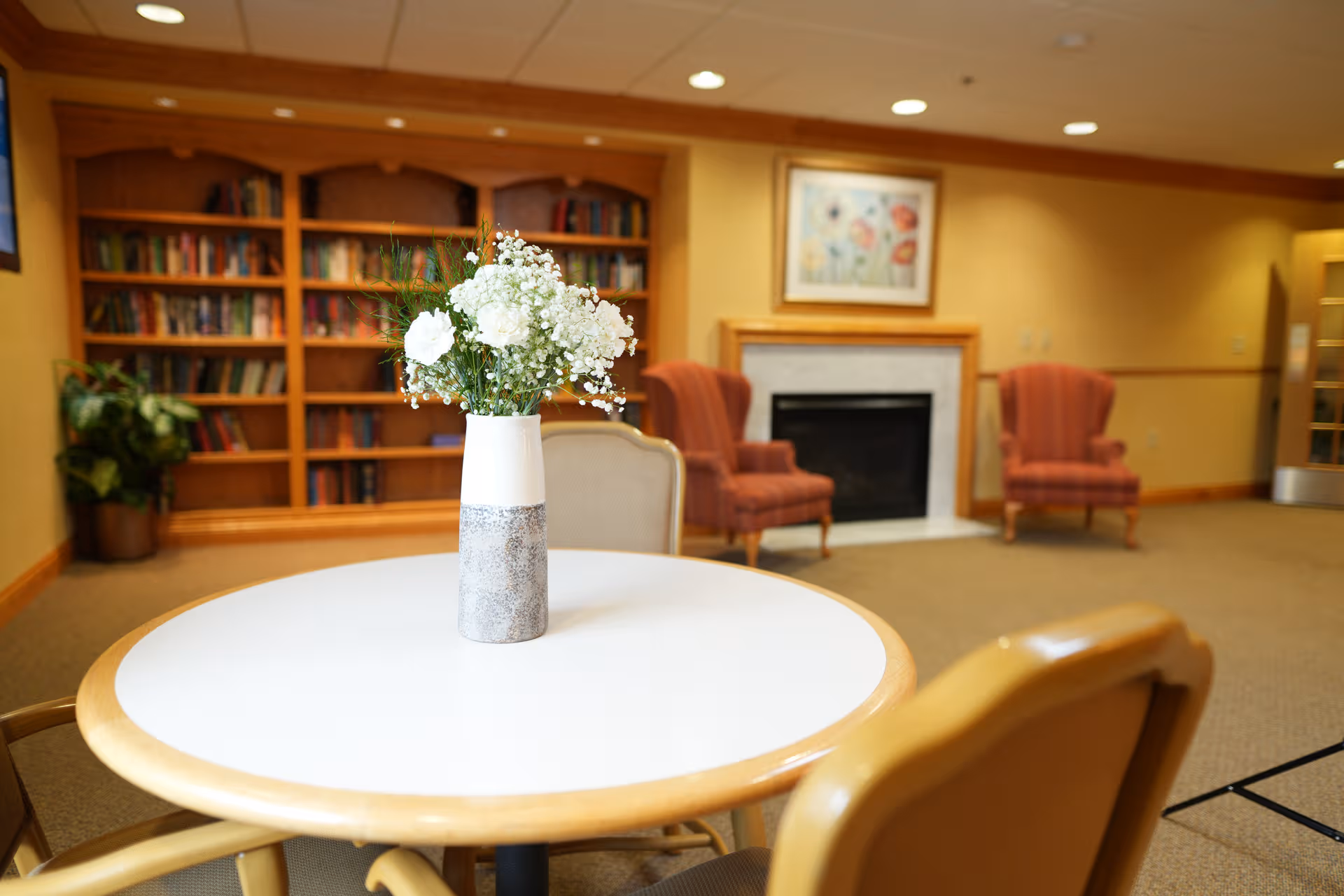 Round table with a vase of white flowers in a cozy lounge with a fireplace.