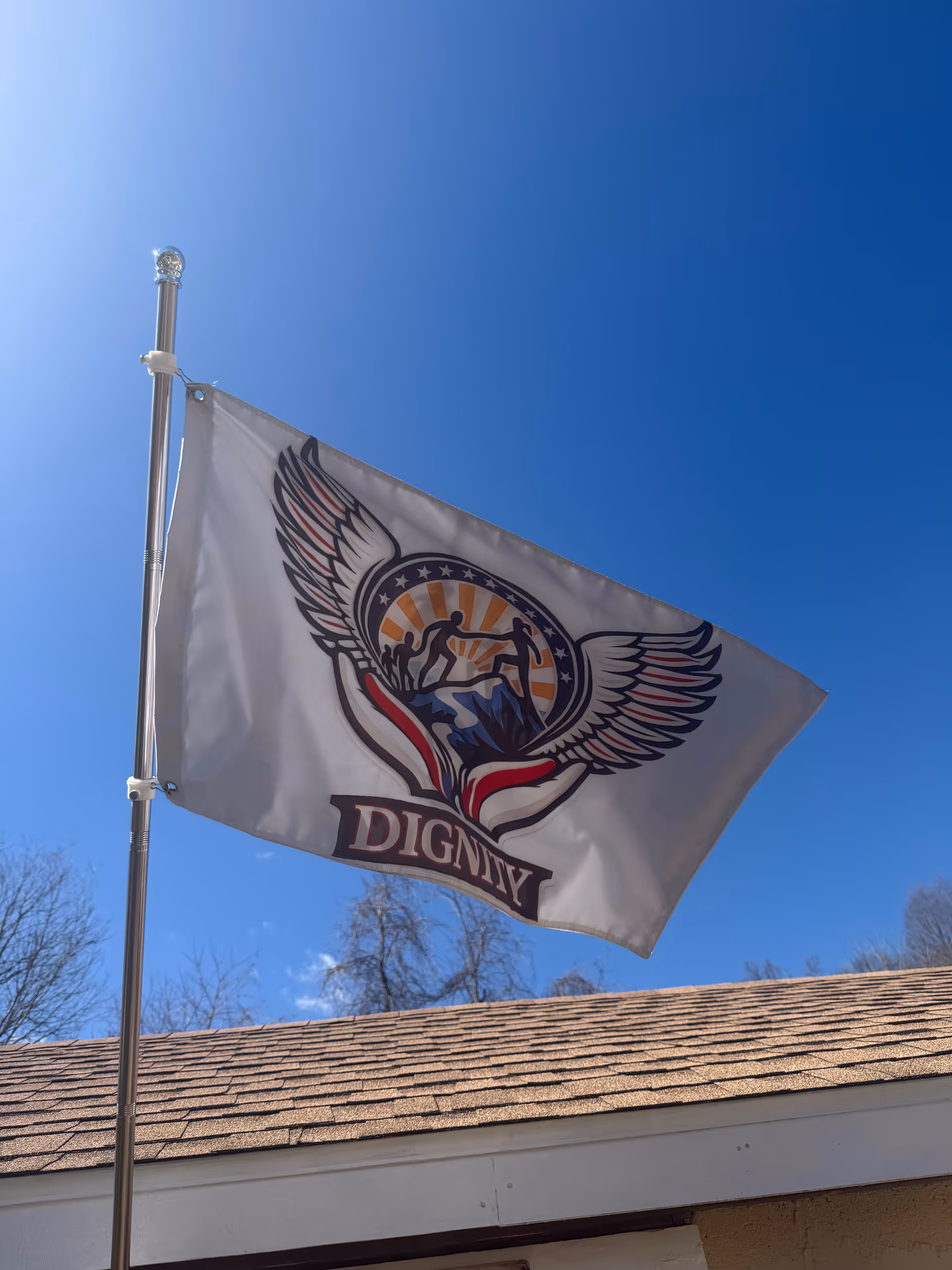 Flag with a winged emblem and DIGNITY flies beside a building under a blue sky.