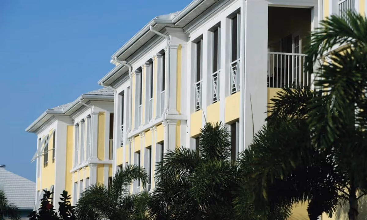 Yellow-and-white multi-story residential building facade with balconies and palm trees in the foreground.