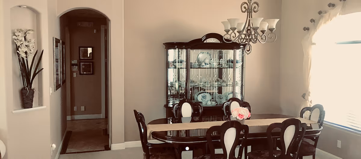 Dining room with glass table, ornate chairs, china cabinet, and chandelier.