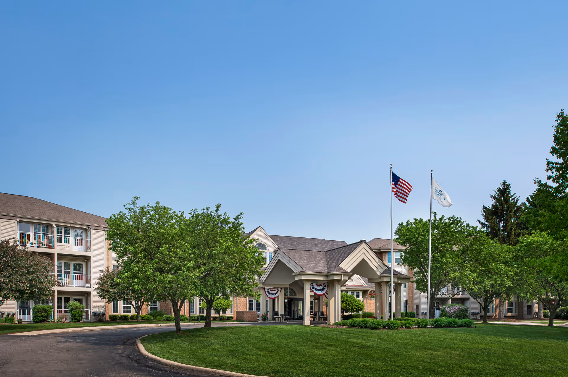 Exterior view of Baldwin House Senior Living Oakland entrance with flags and manicured lawn
