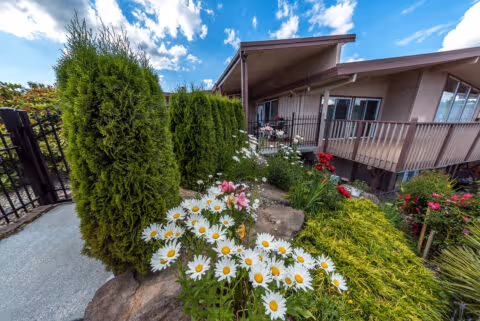 Front exterior of a senior care residence with a landscaped garden and covered entrance.