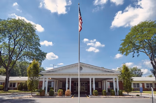 Front view of Cornell Hall Care & Rehabilitation Center with flagpole and trees.