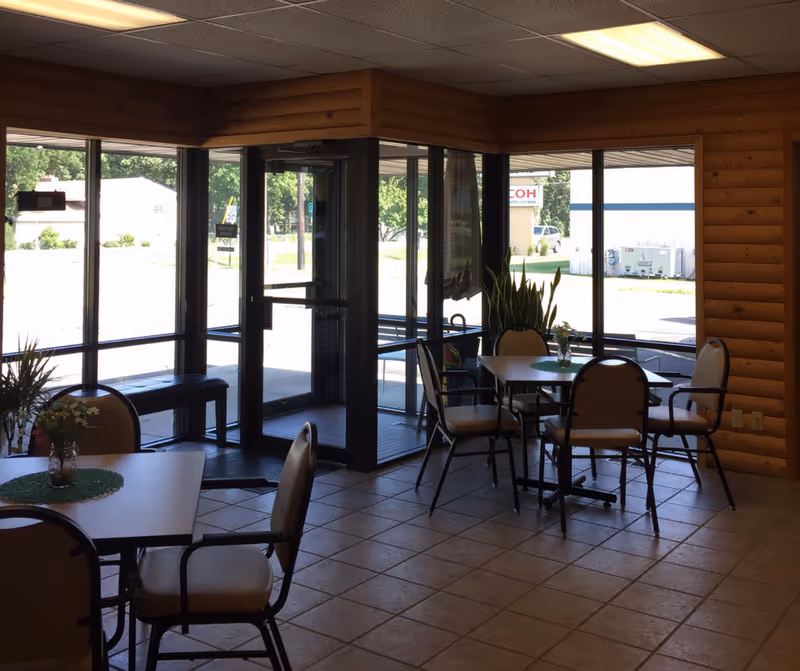 Sunlit dining area inside a wooden-walled facility with glass doors and plants.