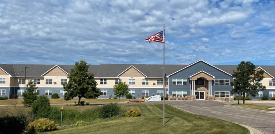 Wide view of Caldwell senior living facility exterior with flagpole, entrance, and manicured lawn.