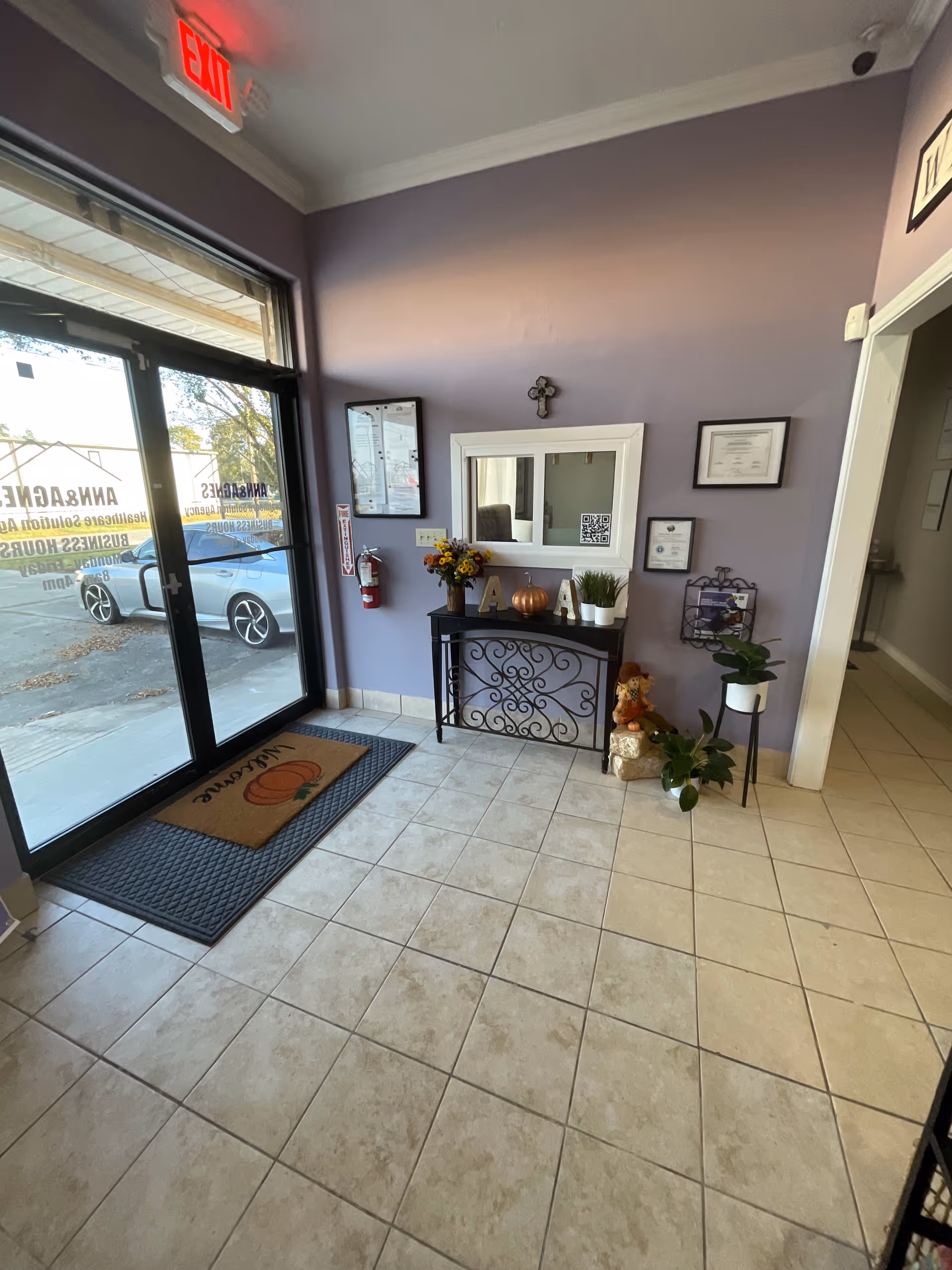 Lobby entrance with glass doors, purple walls, a decorative console table, and plants.