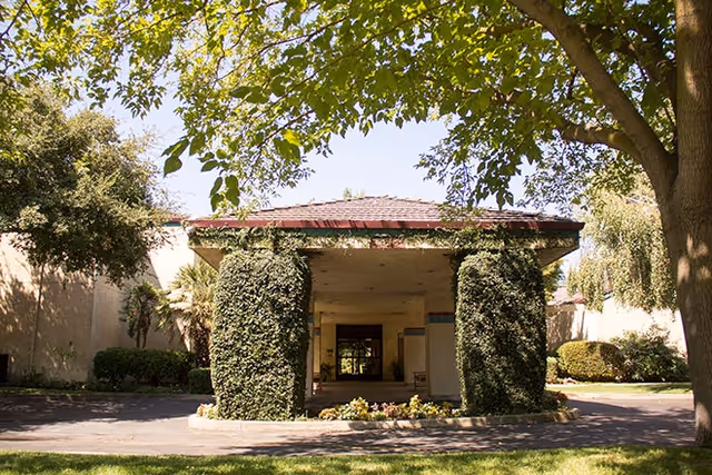 Exterior view of a building entrance with ivy-covered columns and lush trees.