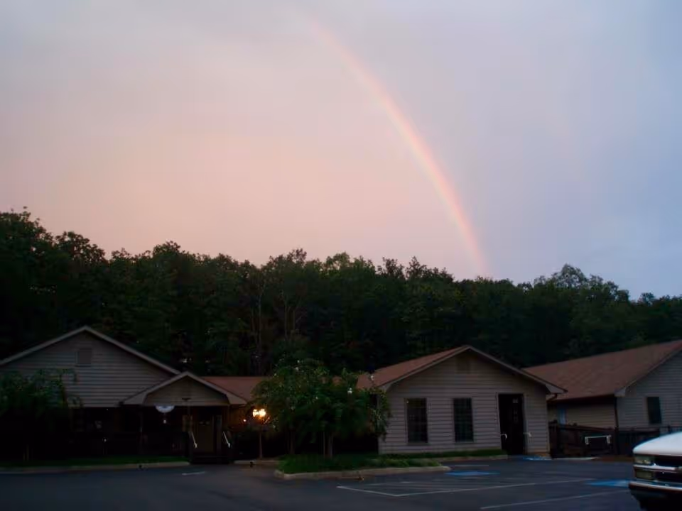 Rainbow arches over Pleasant Valley Personal Care front buildings and a parking lot.