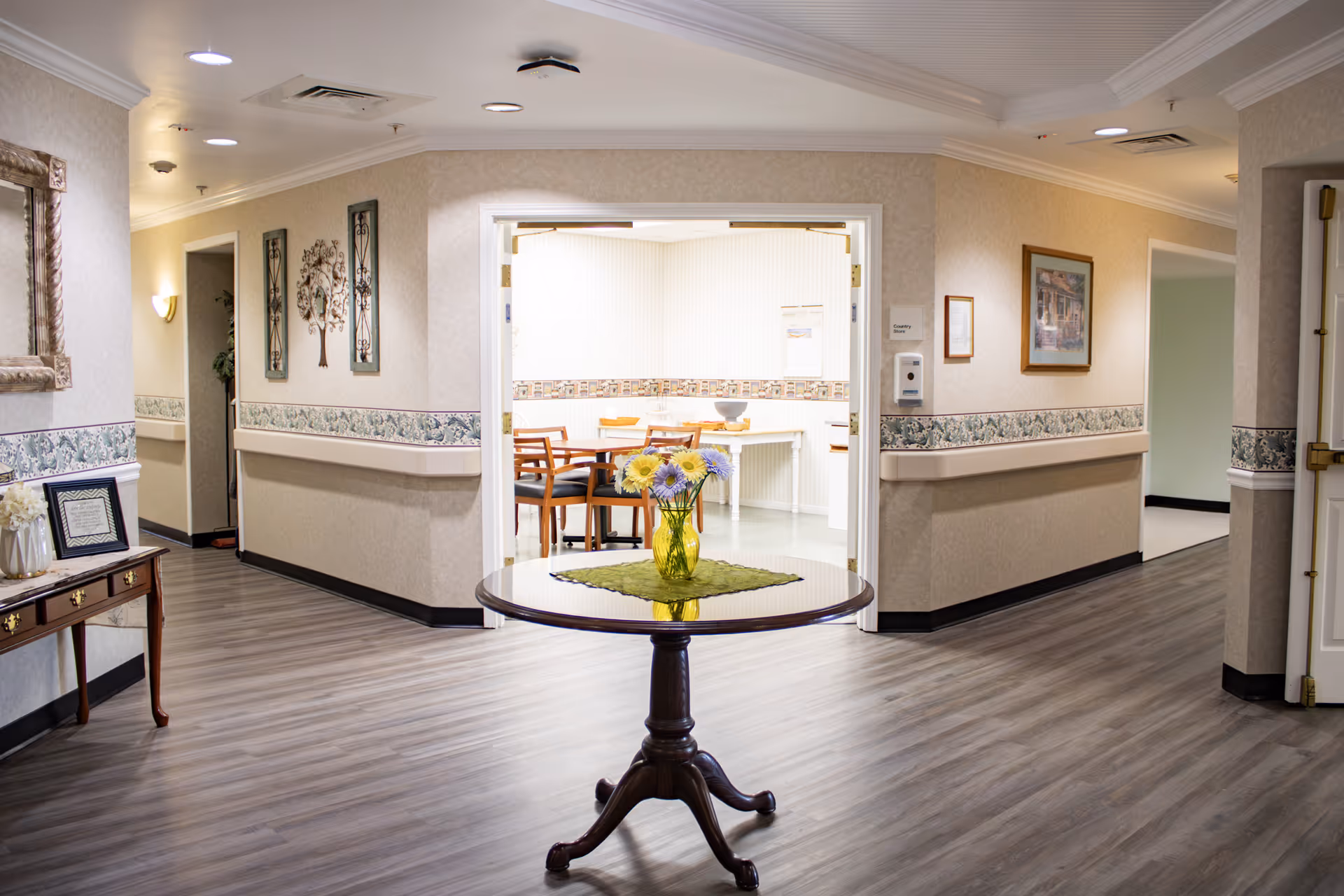 Sunlit hallway in a senior living facility with a round table and floral centerpiece.