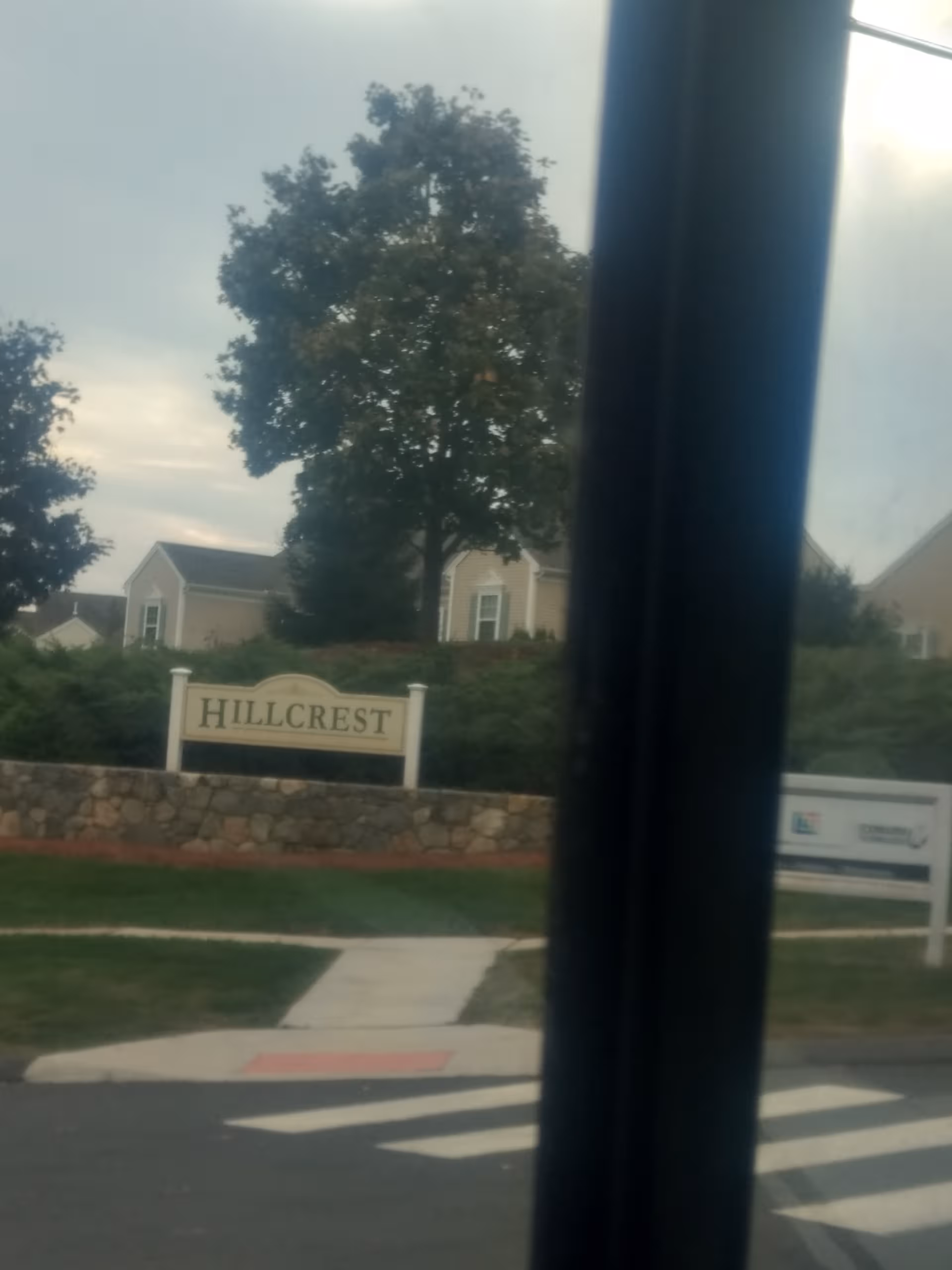 Exterior view of Hillcrest sign with stone wall, trees, and clubhouse buildings.