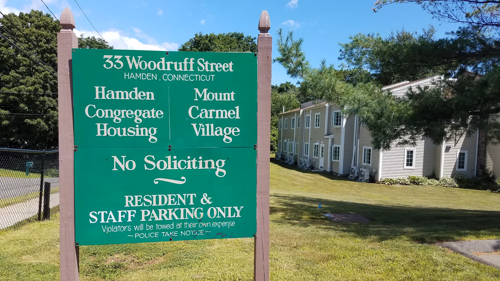 Green sign for Mt Carmel Congregate Housing in front of a beige apartment building.