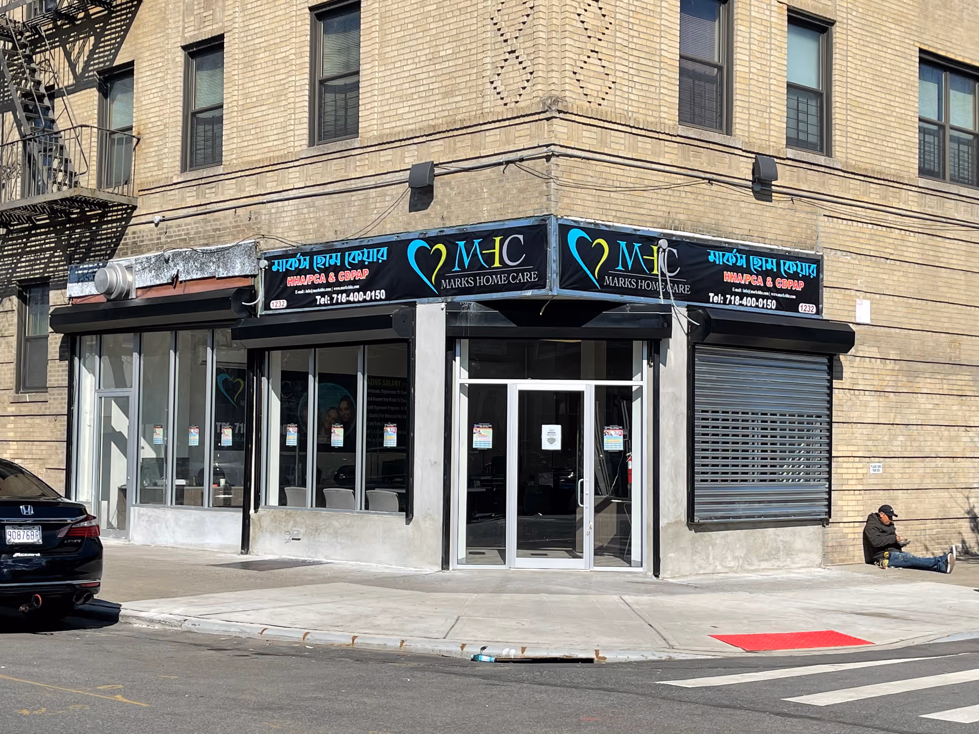 Brick storefront on a street corner displays Marks Home Care signage with a person sitting outside.