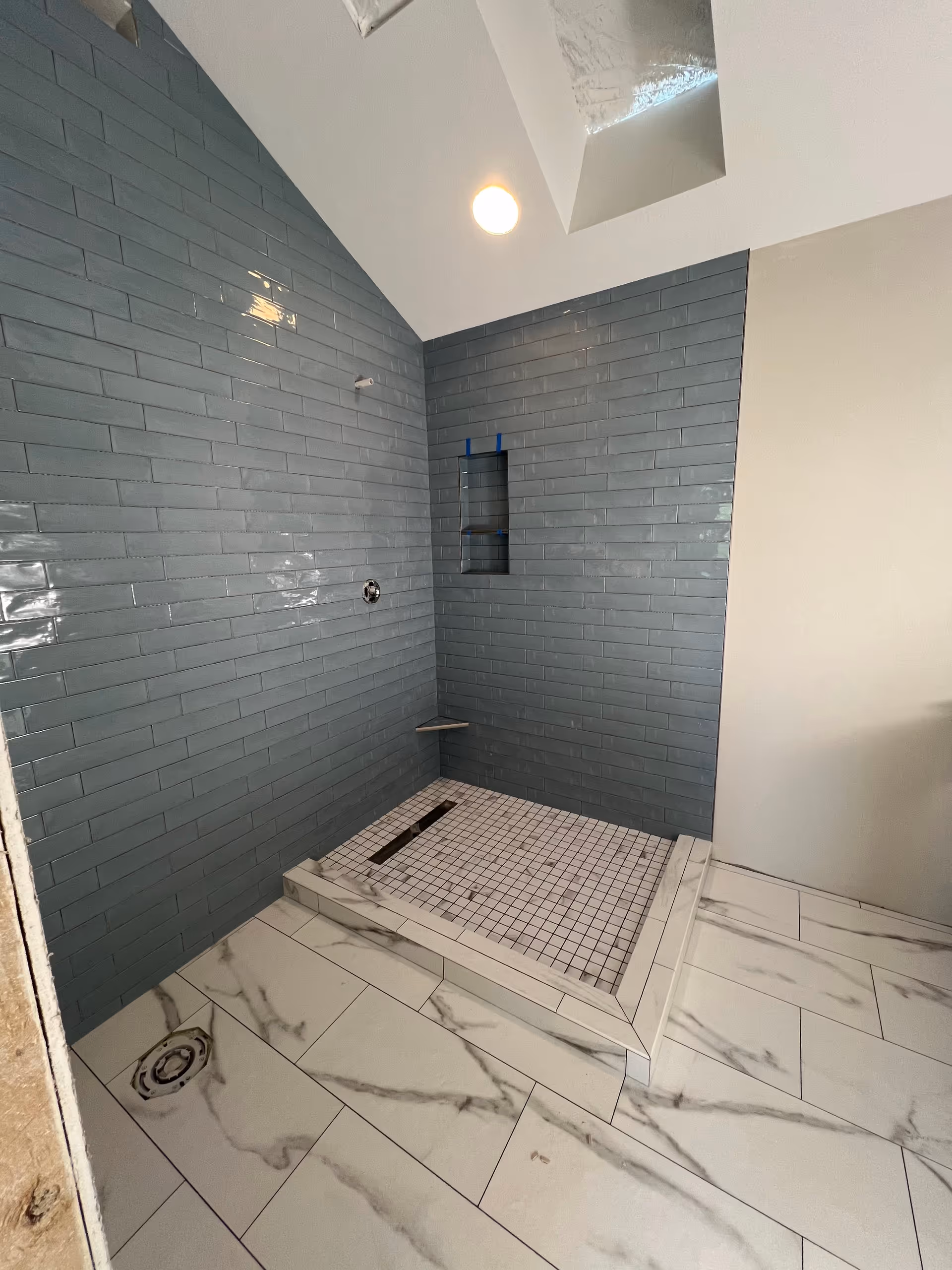 Grey-tiled bathroom shower with built-in bench and marble-patterned floor tiles.