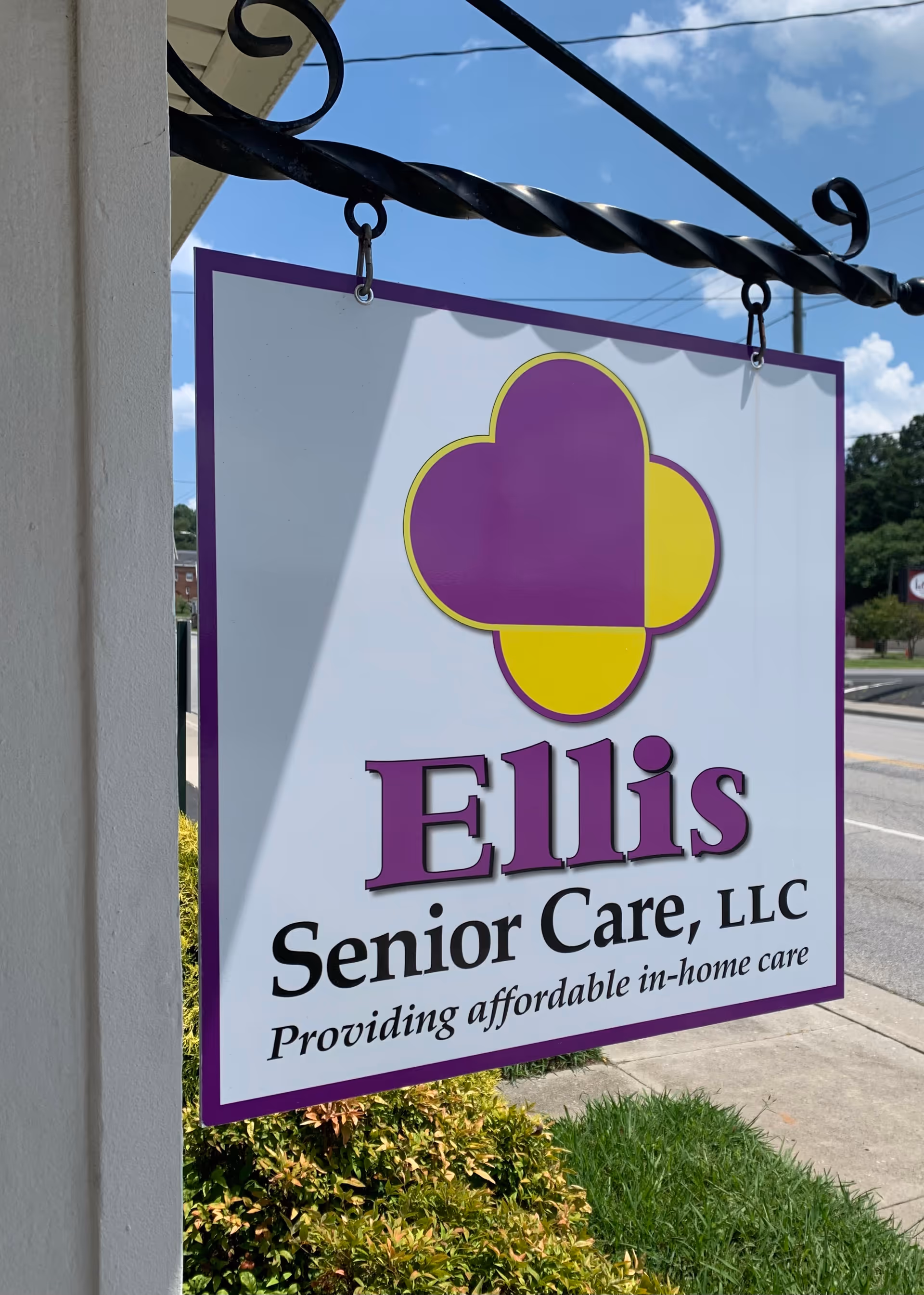 Hanging sign outside Ellis Senior Care, LLC featuring purple-yellow logo.