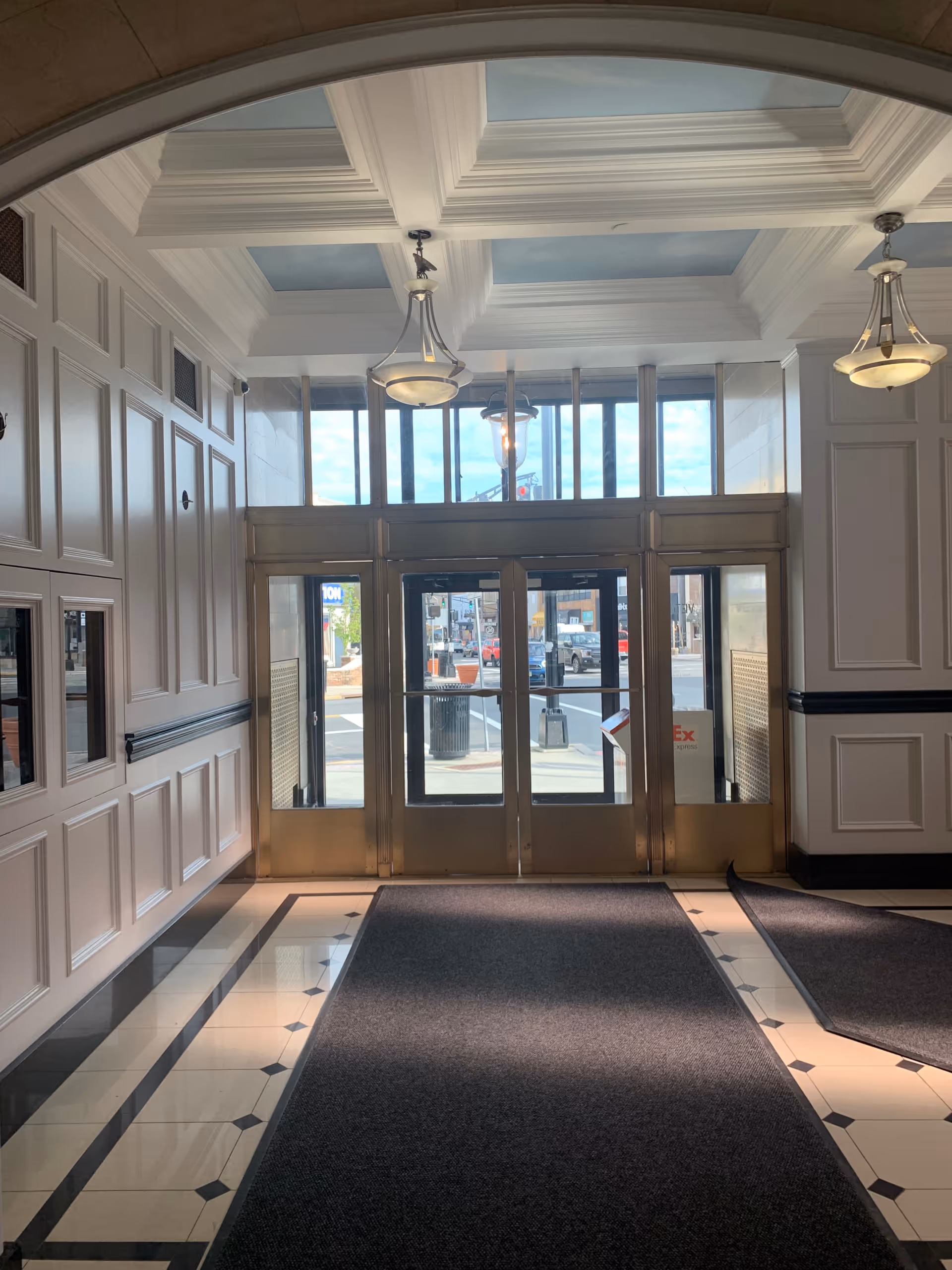 Elegant interior lobby with double glass doors, coffered ceiling, and marble flooring.