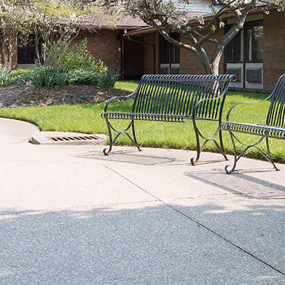 Outdoor seating area with metal benches in front of a brick senior living building.