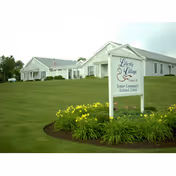 Exterior view of a single-story senior living facility building with a well-maintained lawn and a white sign in the foreground that reads 'Liberty Village Senior Community Assisted Living'.