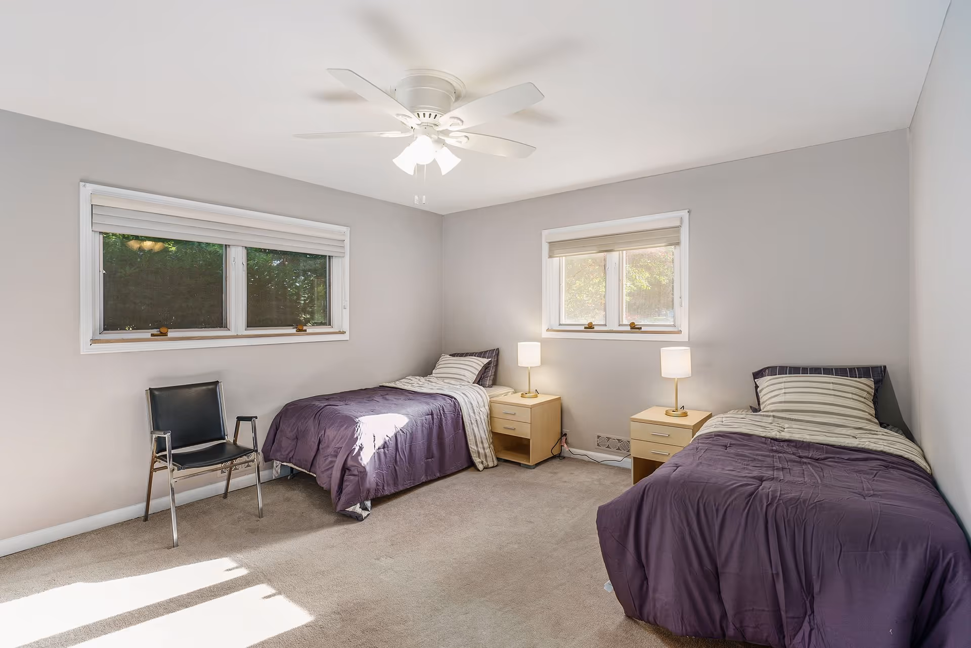Two twin beds with purple comforters and nightstands in a bright, minimalist bedroom.