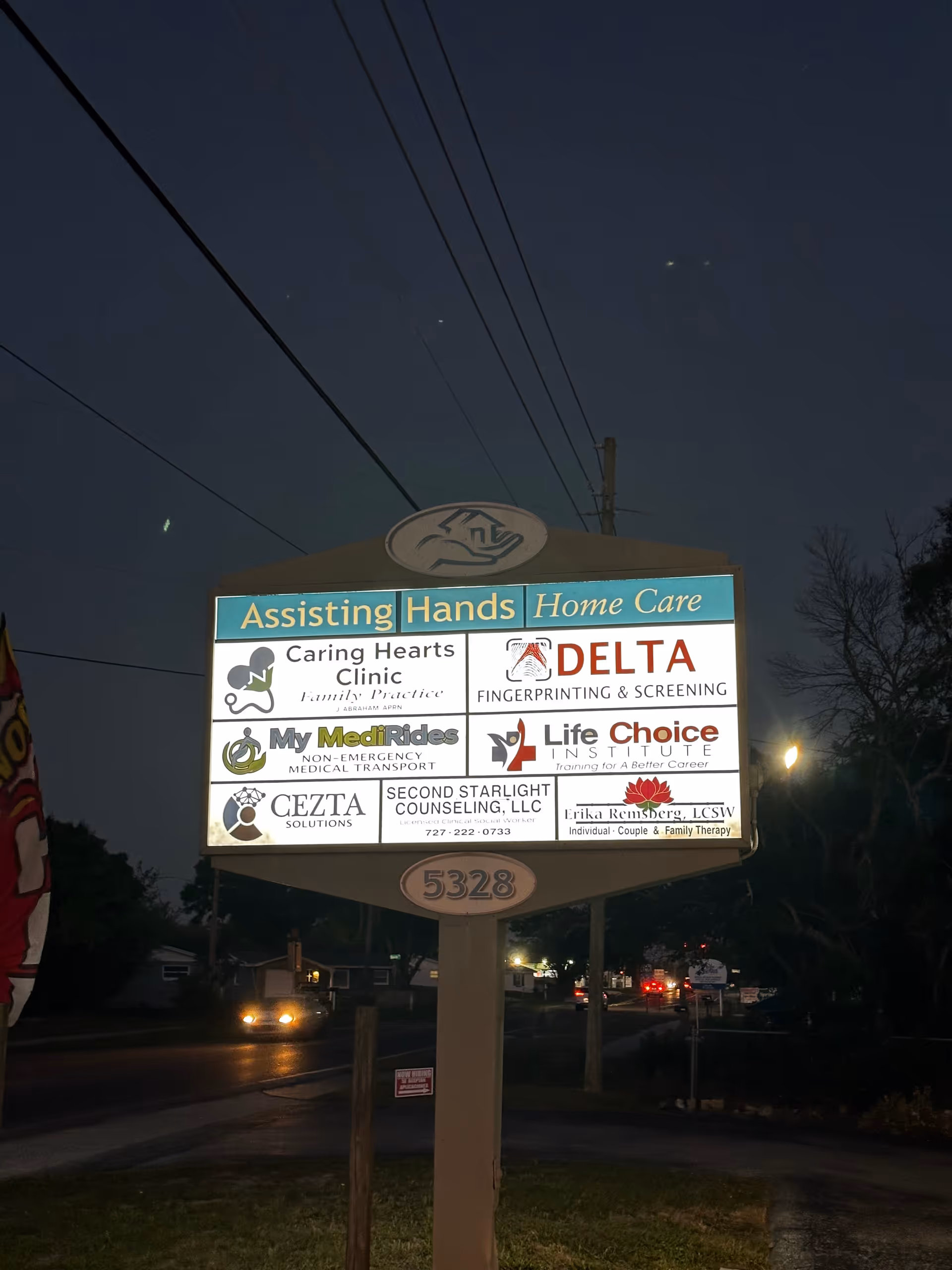 Nighttime exterior signboard for Assisting Hands Home Care displaying various logos.