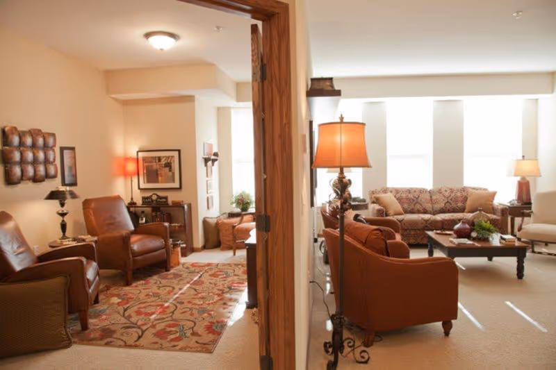 Two adjoining living rooms with leather chairs, sofas, tables, and warm lamps.