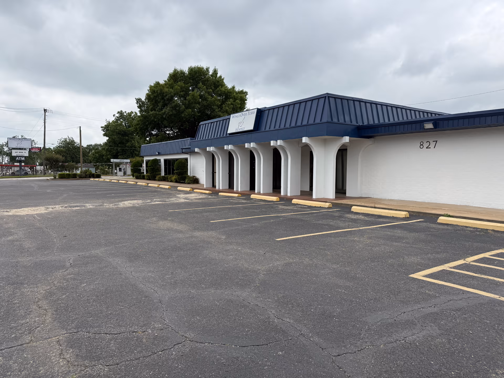 White building with a blue metal roof and arched entryway, set in a large parking lot.