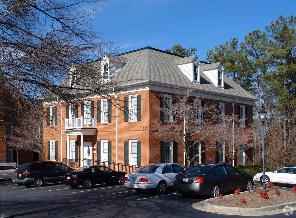 Brick senior living facility with dormer windows, parked cars, and leafless trees in front.