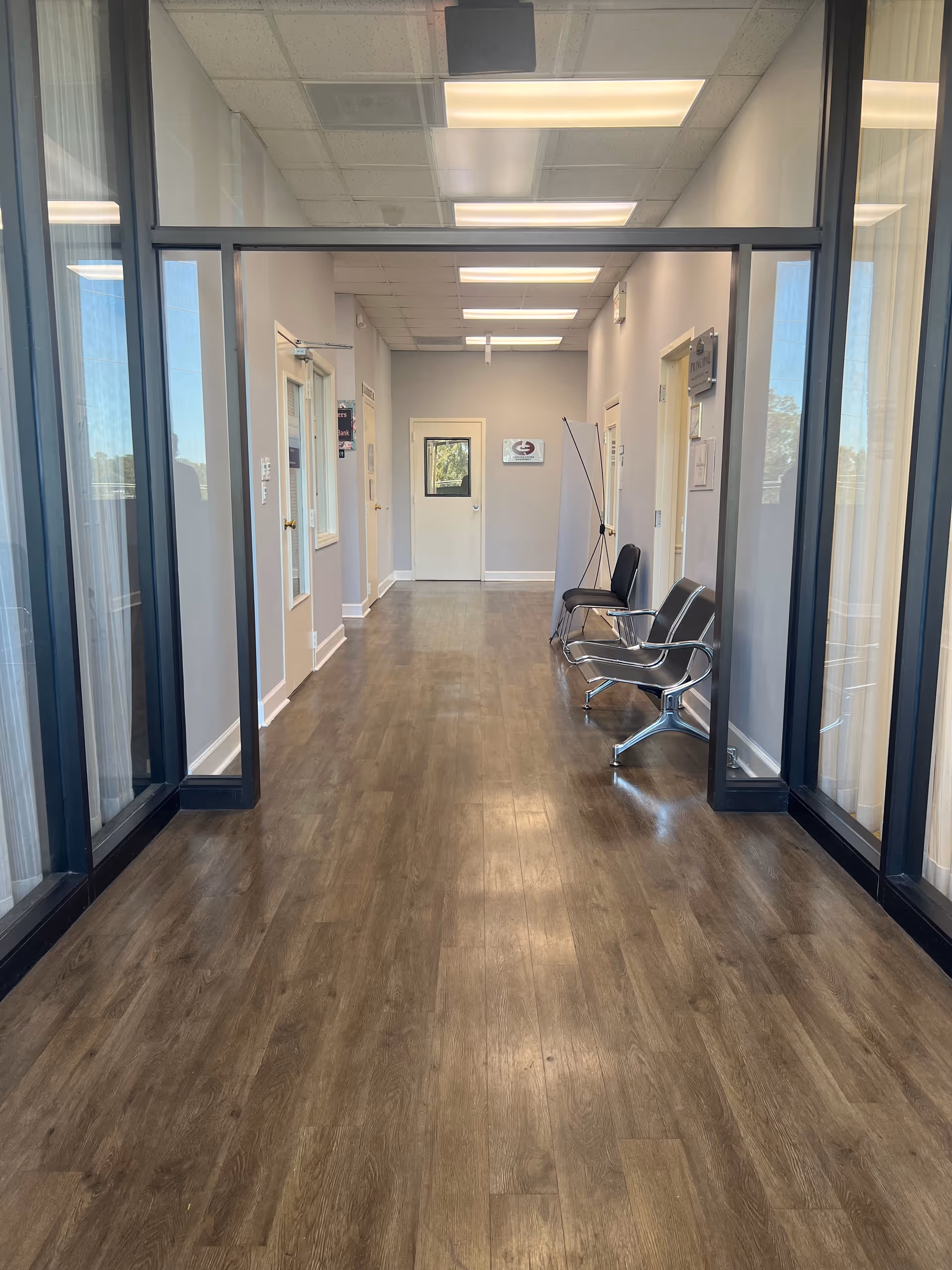 Long hallway in a senior living facility with glass walls, doors, and chairs.