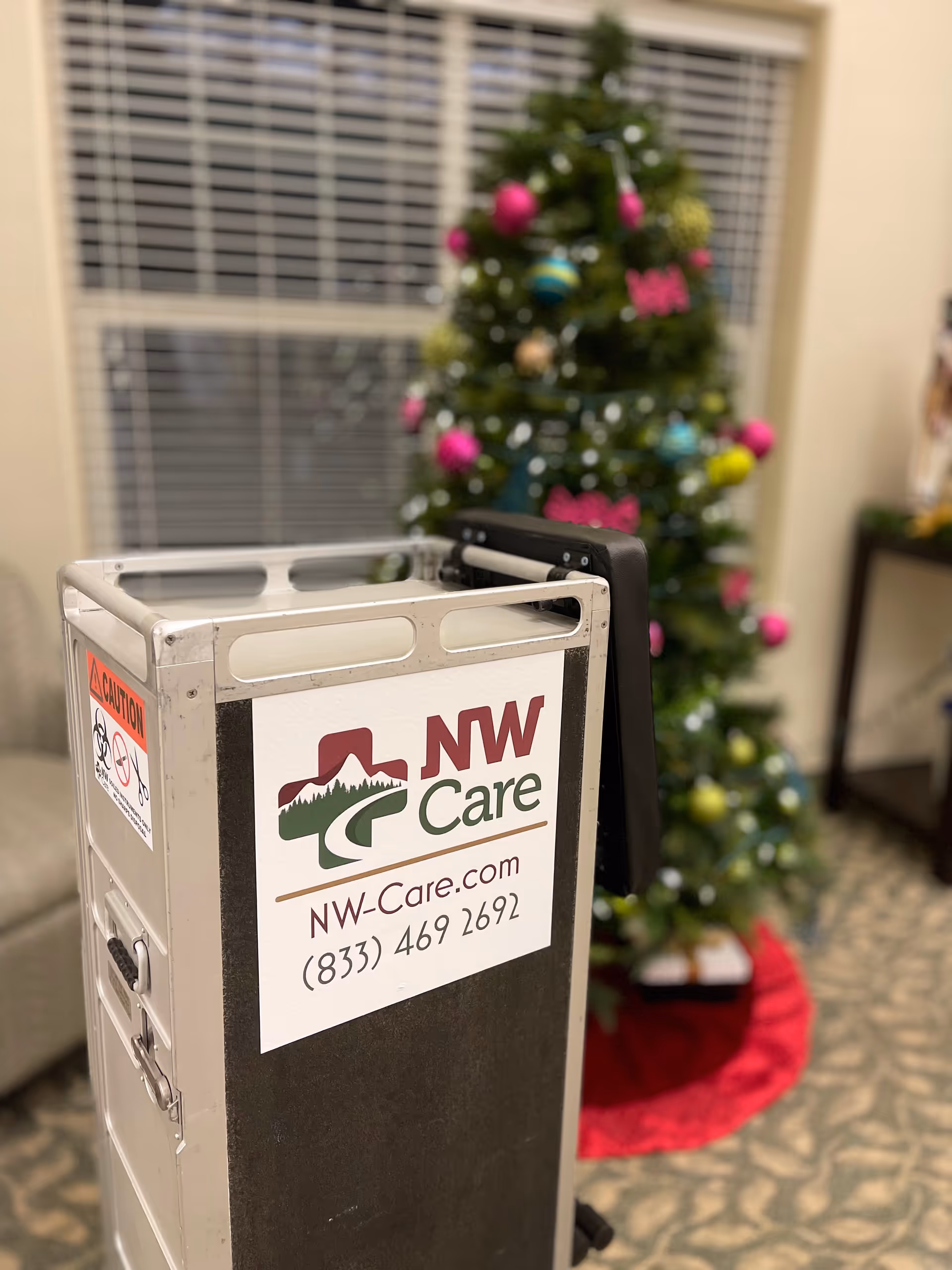 Metal care cart labeled NW Care sits indoors near a decorated Christmas tree.