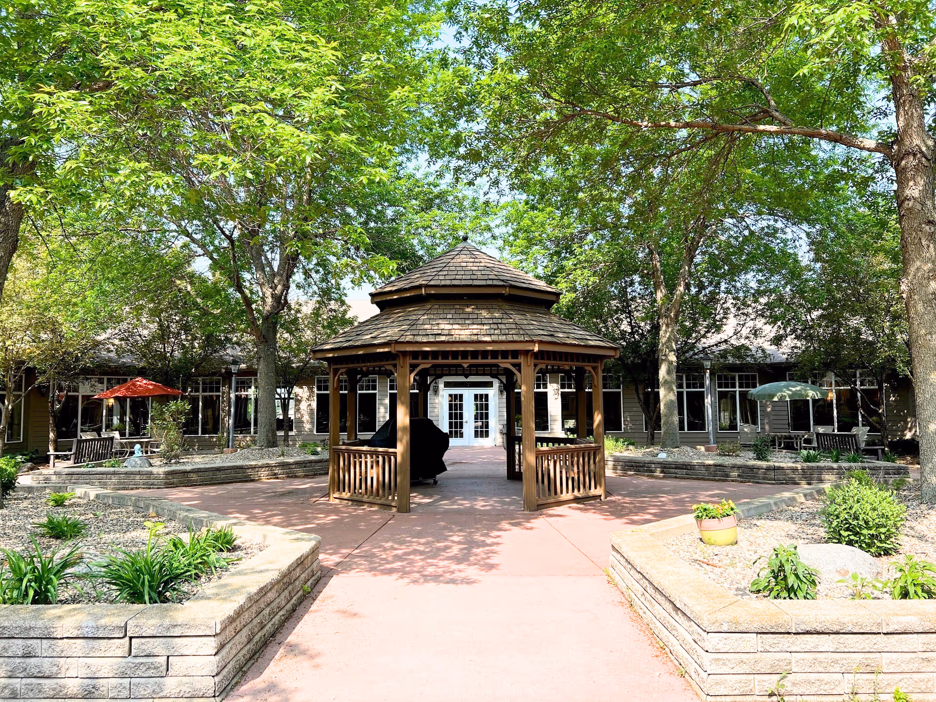 Bethany Meadows courtyard with a wooden gazebo, paved path, benches, and trees.