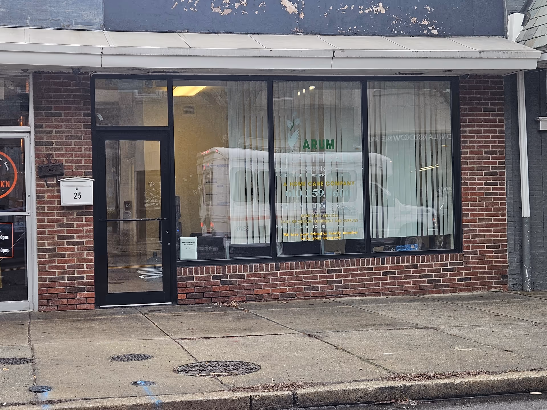 Brick storefront with large glass windows displaying Arum Healthcare Services signage and a parked van.