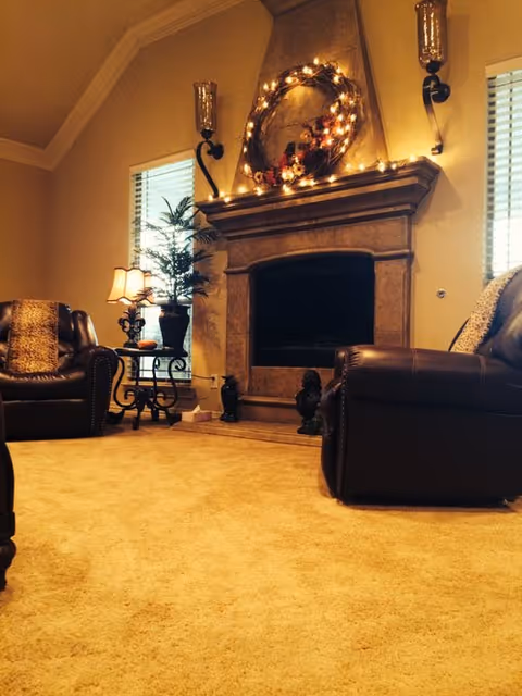 Cozy living room with a lit fireplace, leather seating, side tables, and a decorative mantel.