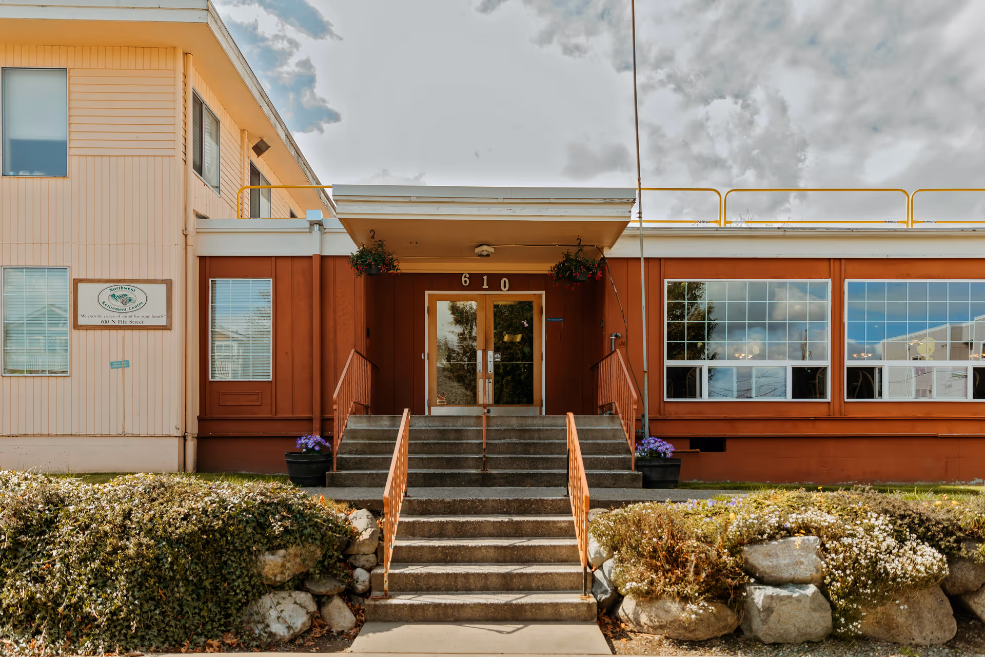 Exterior view of a senior living facility entrance with steps and large windows.