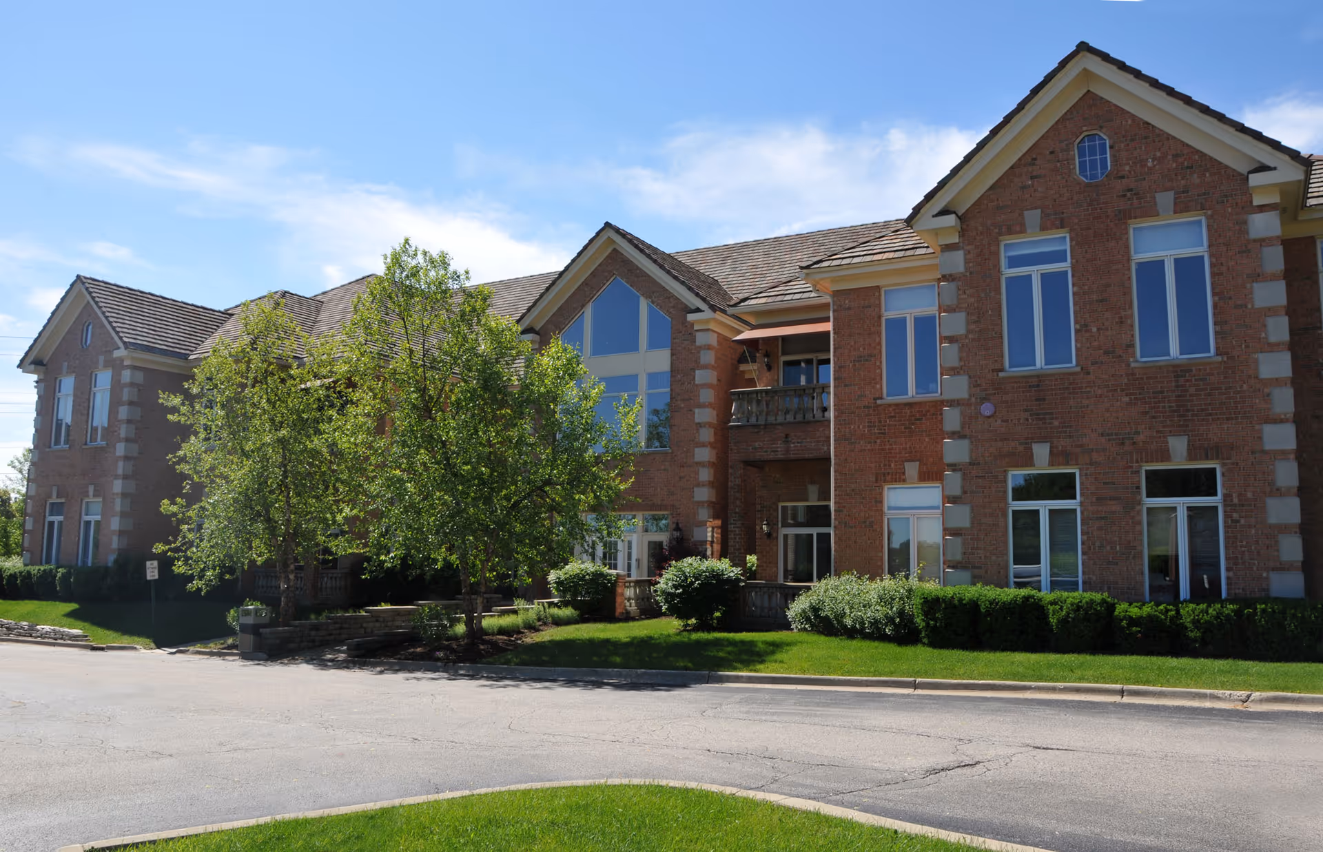 Brick senior living facility with large windows, trees, and a landscaped front entrance.