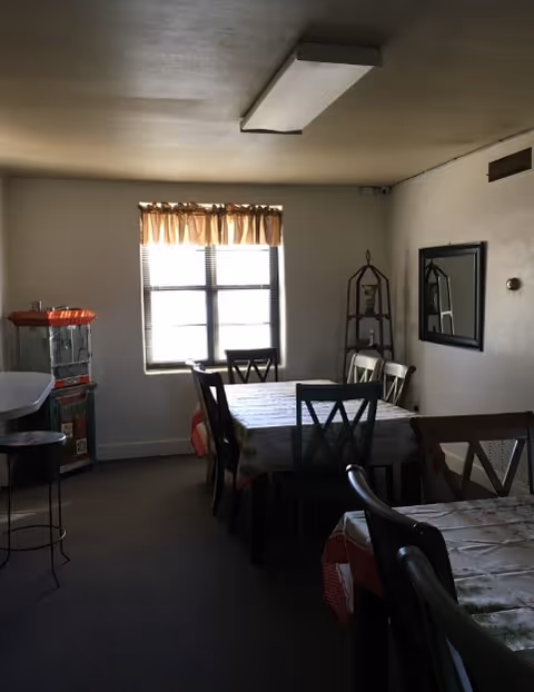 A small dining room with tables, chairs, a window, and a vending machine.
