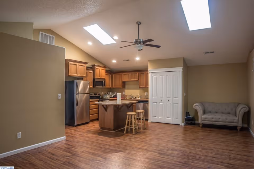 Open-concept kitchen with island, wooden cabinets, stainless steel appliances, and a nearby sofa.