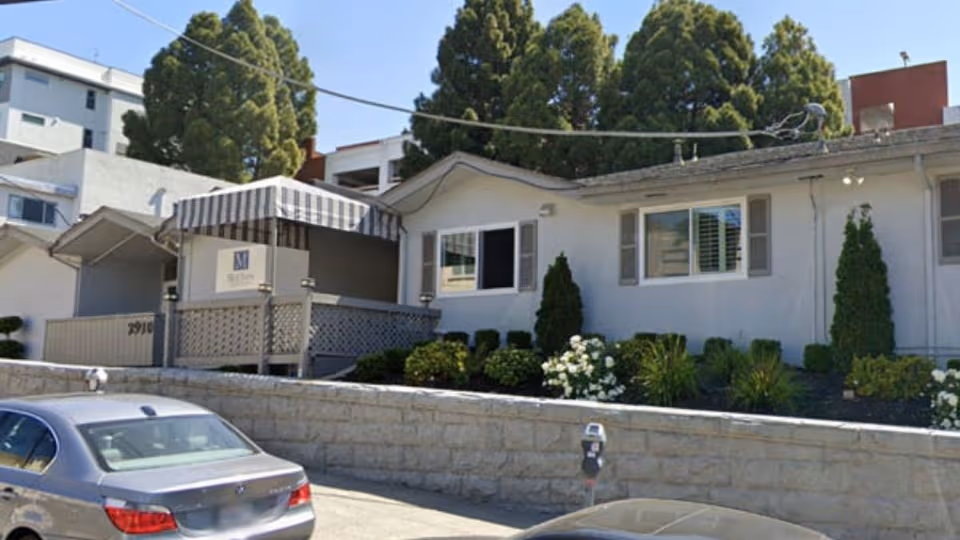 Exterior view of McClure Post Acute building with striped awning, landscaping, and a parked car