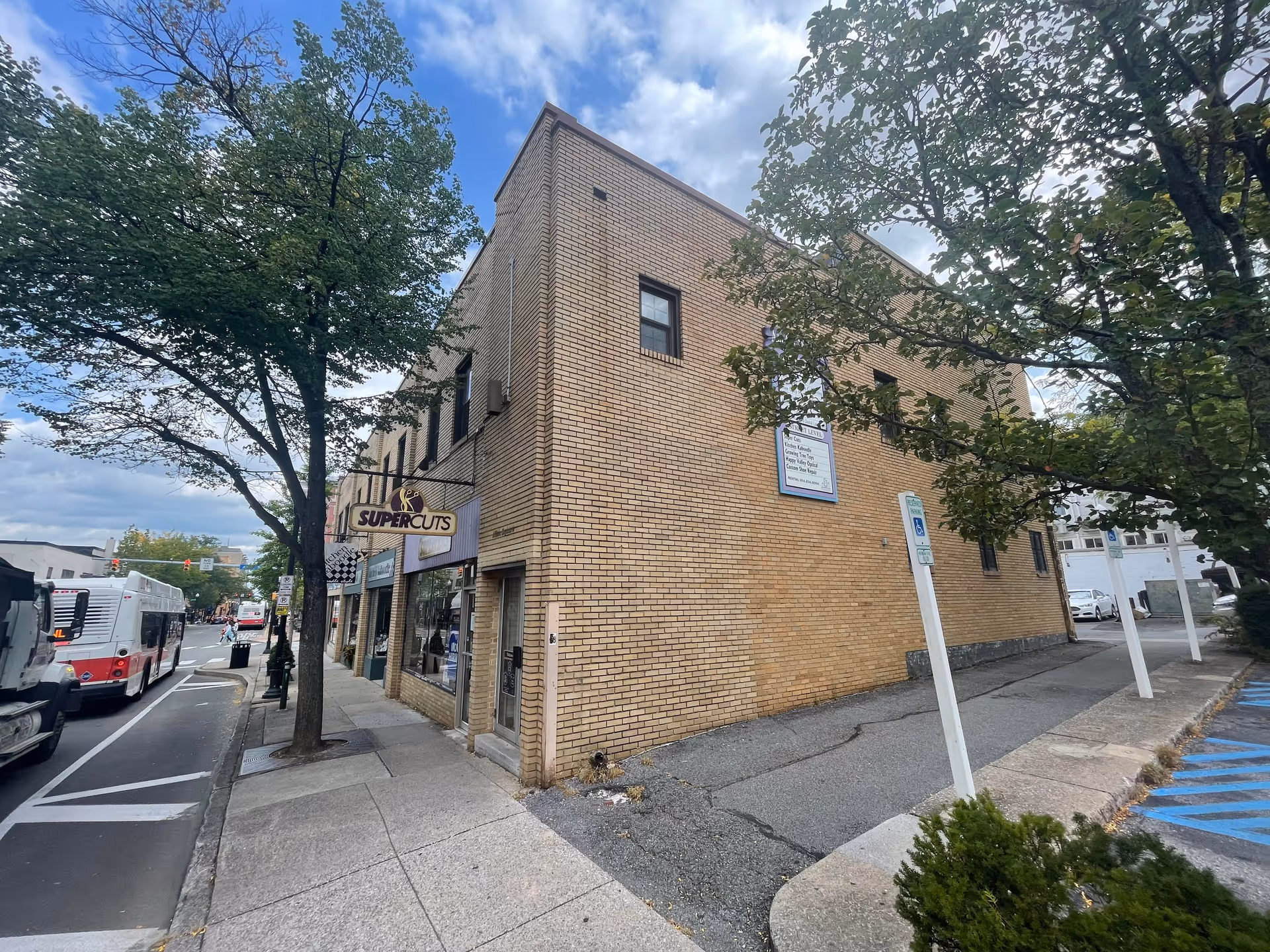 Brick two-story building on a street corner with a Supercuts sign and trees.